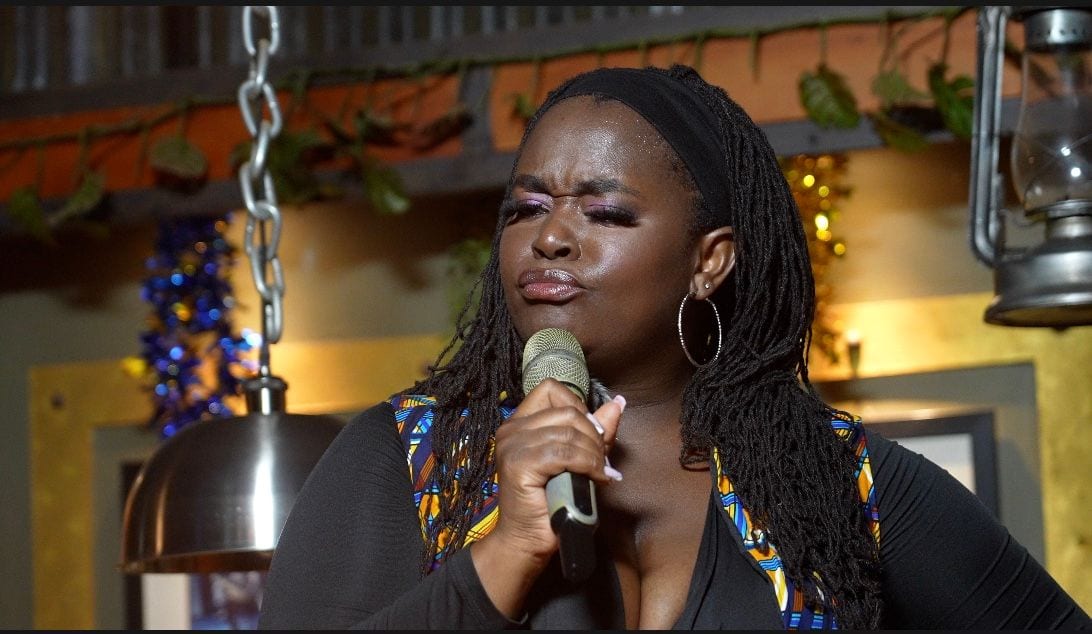 Anyumel Rose, comedian and performer, performing live in East Africa, close-up into a microphone in African print